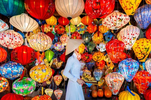 A woman in a white ao dai standing among hanging silk lanterns in a Hoi An lantern shop