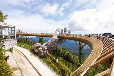 The gold-coloured walkway of the Golden Bridge seen along its length, held by two weathered stone hands