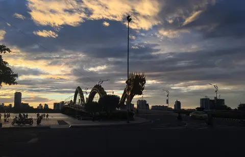 The dragon's head and coiled body of the bridge silhouetted against a cloudy dawn sky