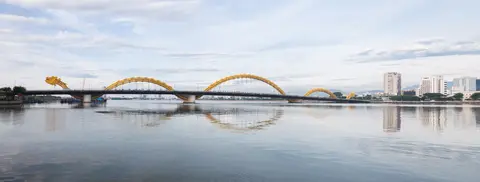 The yellow dragon-shaped bridge stretched across a wide river, city towers along the far bank