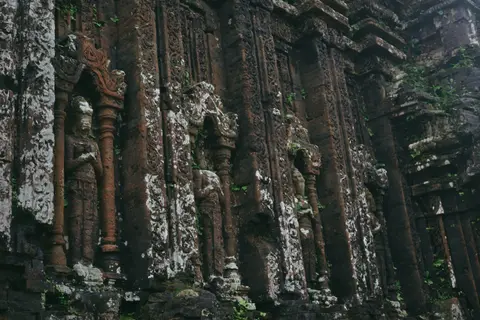 Close view of a weathered brick Cham tower wall with carved pilasters and a niche holding a stone figure