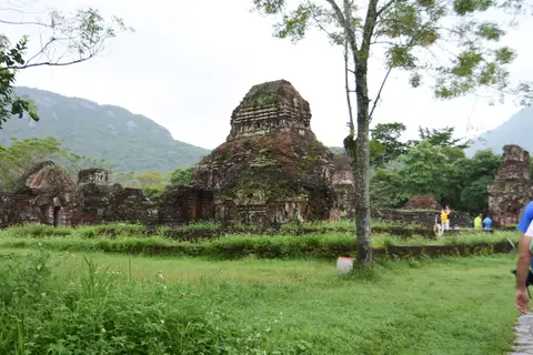 Brick temple ruins across a clearing of grass and trees, with a wooded mountain behind