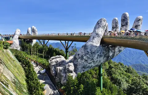 The Golden Bridge crowded with visitors, one stone hand rising above the deck against a hazy sky
