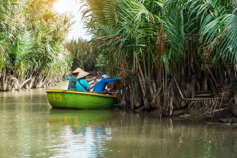 A boatman resting in a small green boat tucked in among the water-coconut palms at the channel edge