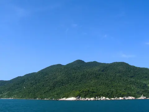 Green island shore meeting clear blue water, with small wooden boats moored off a low settlement