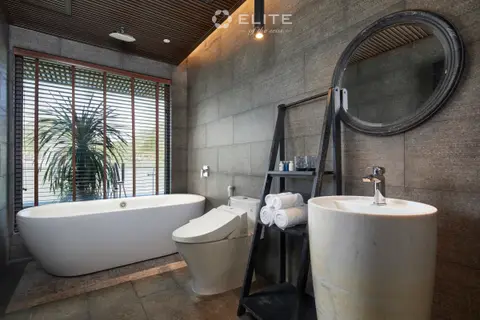 Grey stone cabin bathroom with a freestanding bath, round mirror and shuttered window