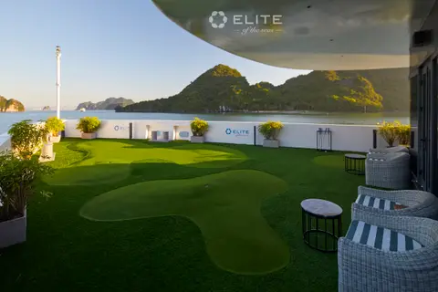 Mini-golf putting green on deck with a flag, wicker stools and a karst rising behind