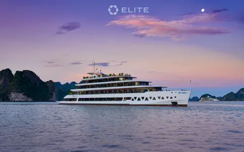The ship lit against a pink and blue twilight sky with karsts on both sides