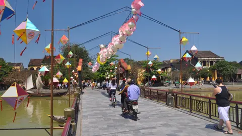 People crossing a footbridge strung with paper lanterns and bunting over the river at Hoi An