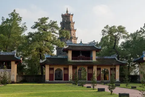 The seven-tiered brick tower of Thien Mu Pagoda rising behind a temple hall and pine trees