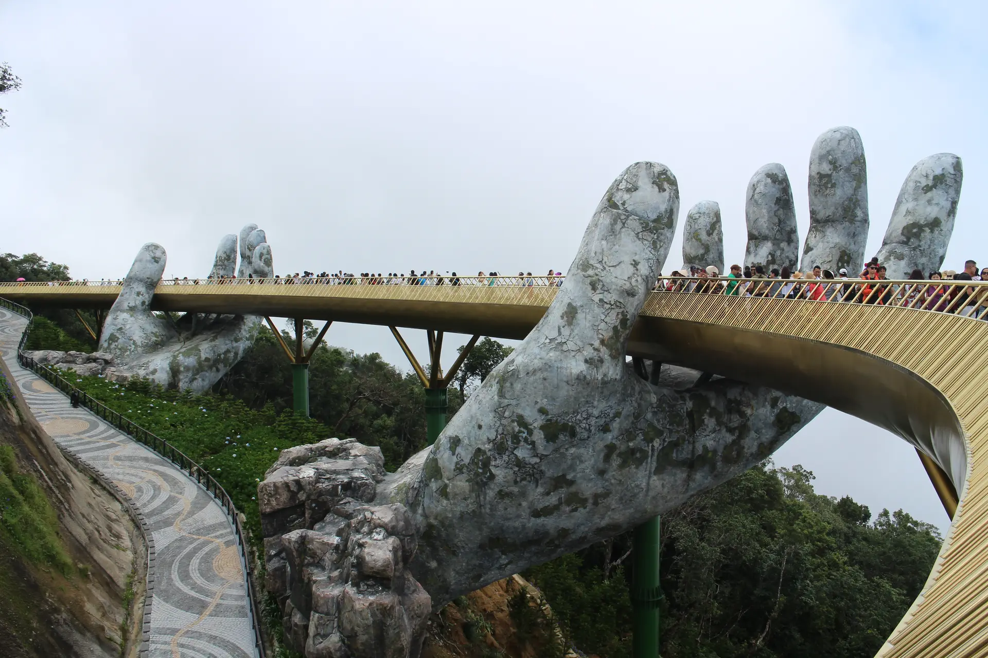 Visitors walking the Golden Bridge between the two stone hands, with wooded hills falling away behind