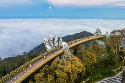 Golden Bridge held up by two giant stone hands, curving above a sea of cloud on a forested ridge