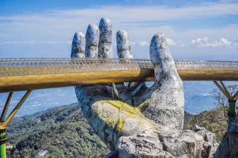 The two weathered stone hands close up, holding the gold walkway above the treetops