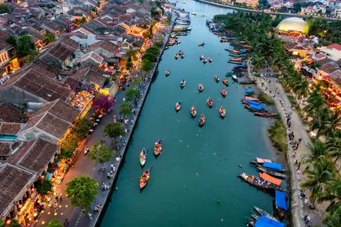 Looking down on the Hoi An river packed with small boats, wakes crossing the green water