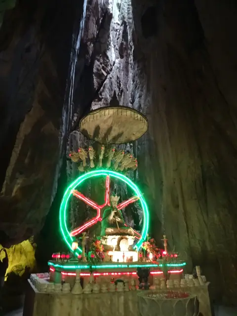Lit shrine deep inside a cave, a ring of coloured lights above the altar and rock walls rising into shadow