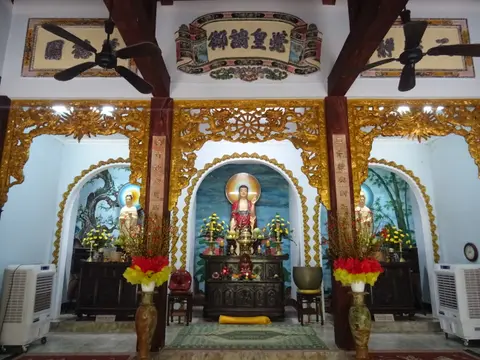 Gilded altar inside a pagoda hall, with red and gold columns and ceiling fans overhead