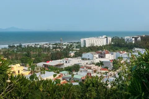 View south-east over the coastline and beachfront buildings from a high viewpoint among trees