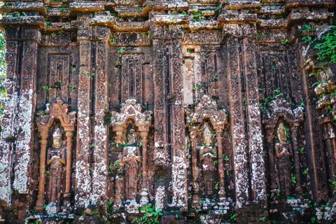 Detail of carved brickwork on a Cham temple facade, with moss and lichen across the mouldings