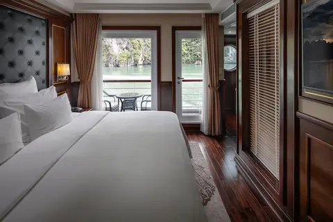 Вид от кровати в каюте Deluxe Balcony через стеклянные двери на приватный балкон с двумя стульями