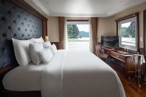Сьют Elegance Balcony с кроватью в белом белье, за ней эркер, напротив — телевизор