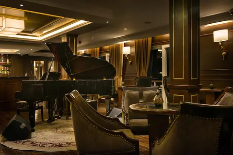 Лаунж Piano Lounge: рояль в дальнем конце, кожаные кресла и низкие столики в теплом свете ламп