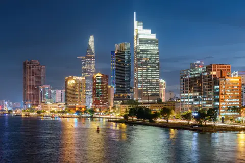 Die Skyline von Ho-Chi-Minh-Stadt entlang des Flusses in der Abenddämmerung, Türme beleuchtet und im Wasser gespiegelt