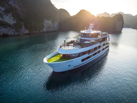Stellar of the Seas seen head-on at sunrise, moored between limestone karsts on calm water
