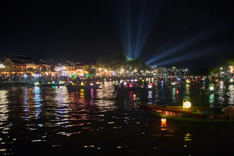 挂满发光灯笼的船只行驶在黑暗的河面上,色彩在水中倒映成双,夜色中格外醒目