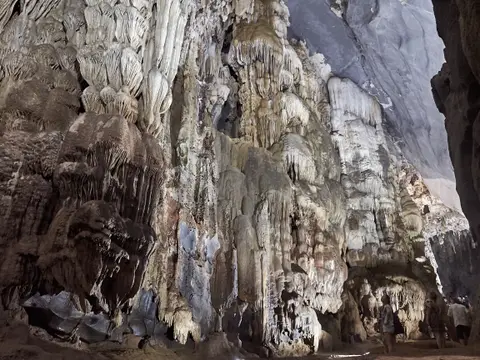 溶洞内灯光照亮的石灰岩壁和悬挂的钟乳石，前景水面黑暗